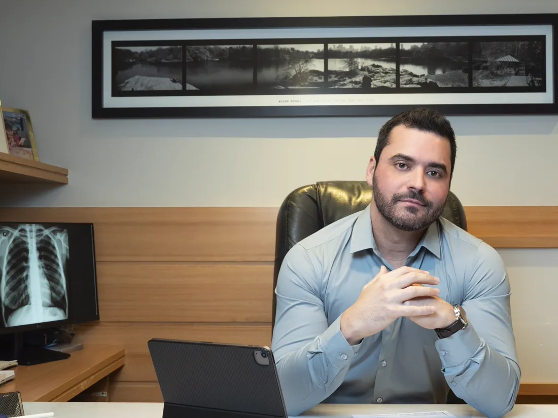 Dr. Marcio Machado no consultório, com um raio-x de tórax na tela ao lado